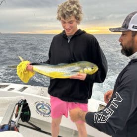 A young angler proudly displaying a vibrant Mahi Mahi while fishing on a charter boat, with a scenic ocean backdrop.