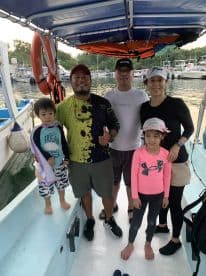 A family of four enjoying their fishing trip aboard a boat, with children present and a scenic marina backdrop.