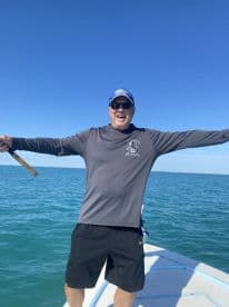 A joyful angler celebrating on the bow of a boat, showcasing the excitement of fishing in clear blue waters.