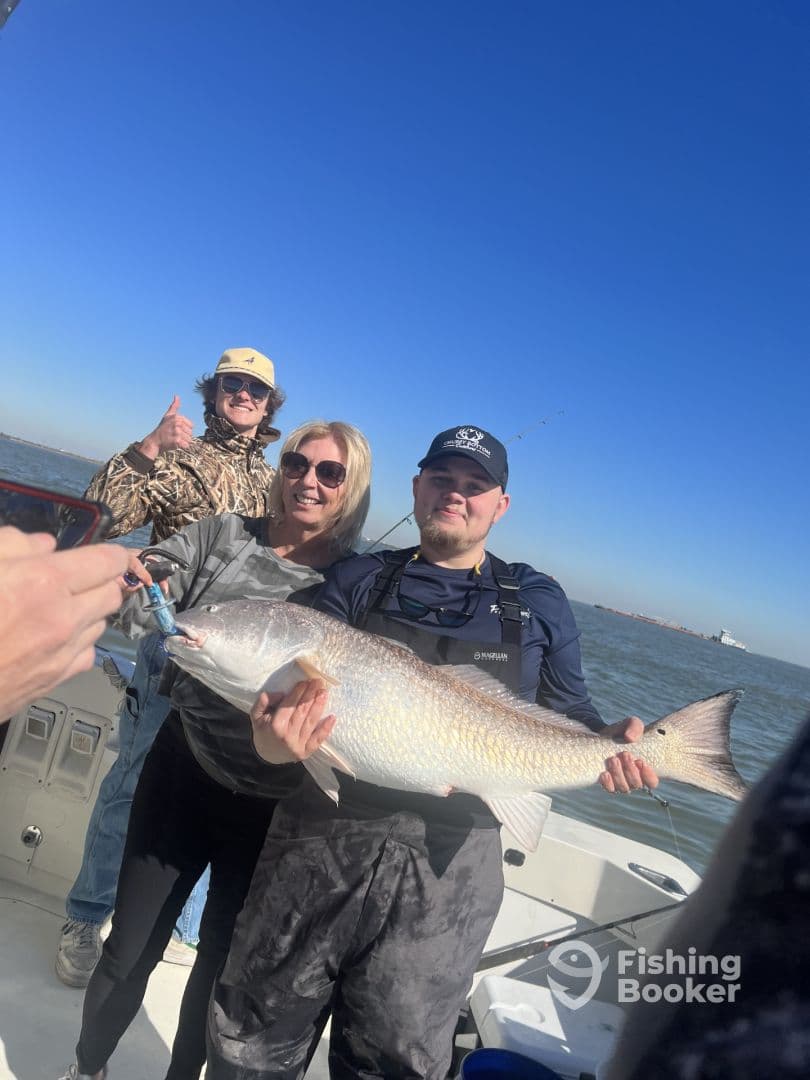 Group of anglers celebrating a successful catch of a large Redfish while on a fishing charter.