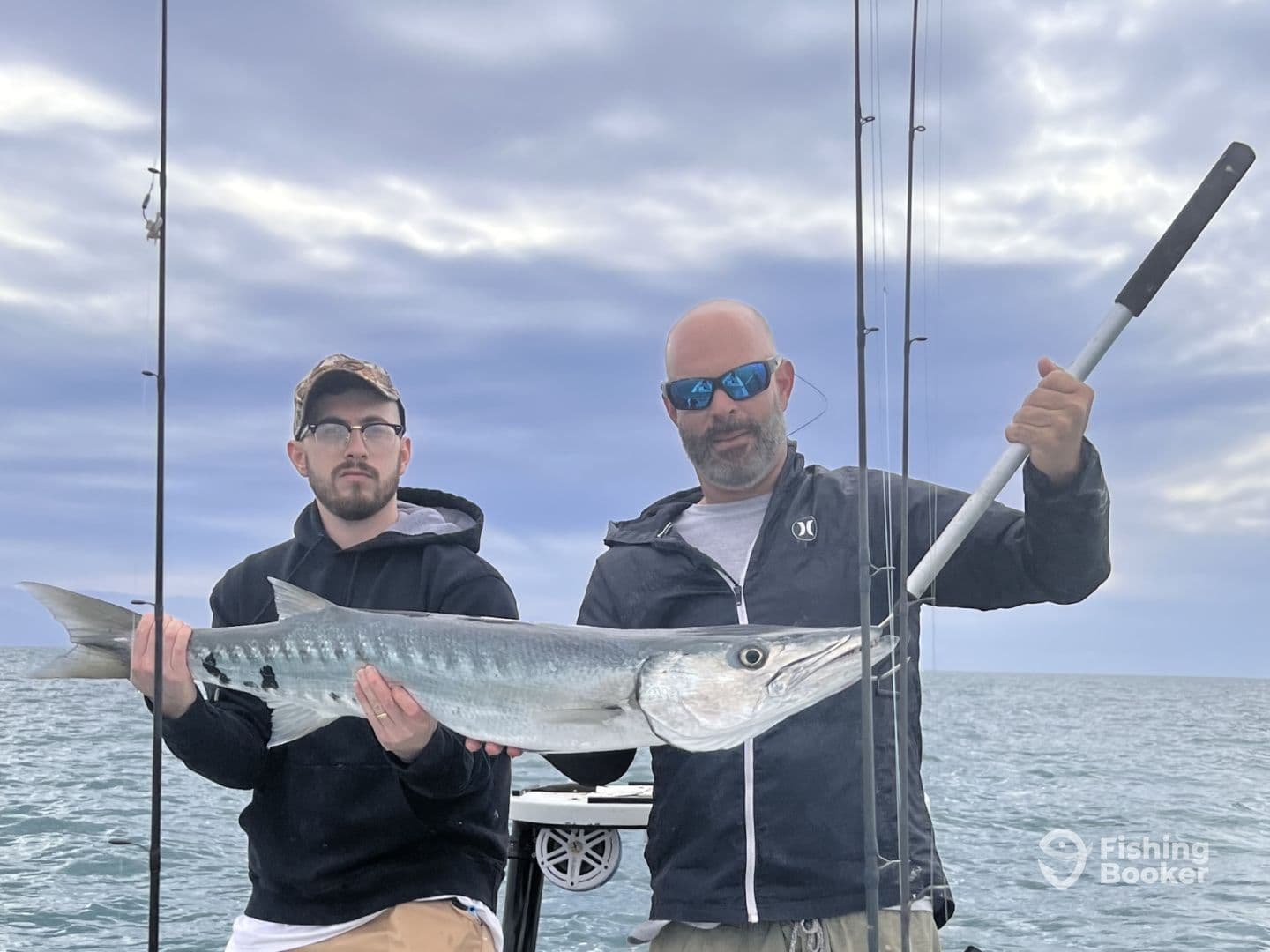 Two anglers proudly displaying a large Barracuda while fishing offshore, showcasing their successful catch in a scenic ocean setting.