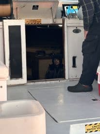 A young child peeks out from the cabin of a fishing boat, while an adult stands nearby, showcasing the interior space.