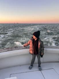 A young boy enjoying the boat ride, looking out at the sunset over the water, showcasing a peaceful fishing environment.
