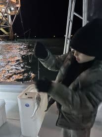 A young angler is reeling in a fish while fishing at night near an offshore platform, showcasing the excitement of the catch.