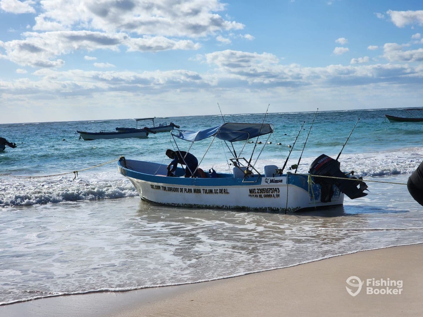 A small fishing boat anchored on the beach with fishing rods visible, set against a backdrop of clear blue waters and a sunny sky.