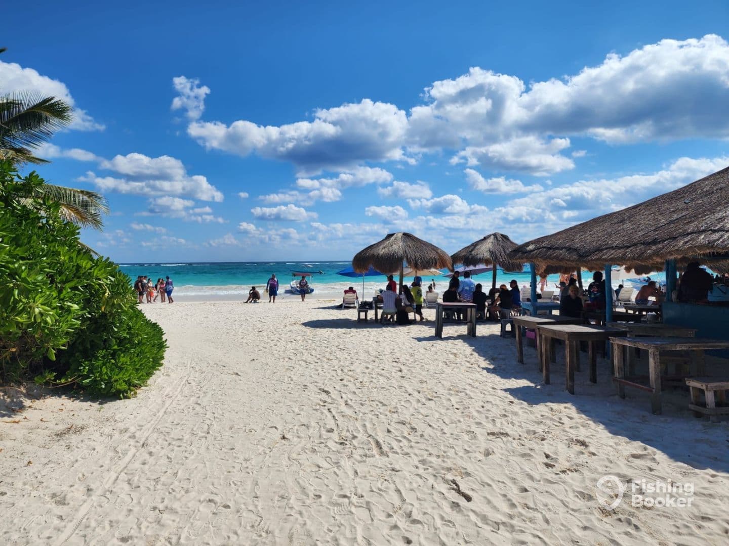 A vibrant beach scene with people enjoying the sun and sand, featuring thatched umbrellas and a clear blue sky.