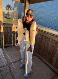 A proud angler displaying two large Redfish at a coastal fishing location, showcasing a successful day on the water.