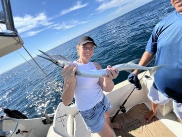 An angler proudly displaying a Barracuda while fishing on a sunny day in open waters.