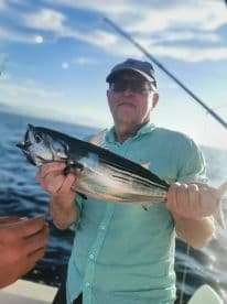 An angler proudly displaying a freshly caught Tuna while fishing offshore, showcasing a beautiful day on the water.