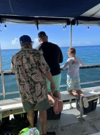 A family enjoying a fishing trip on a boat, with a child seated on the edge, looking out at the ocean.