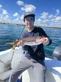 Angler holding a vibrant Snapper while fishing from a boat in clear blue waters, showcasing a successful day on the water.