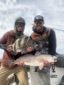 Two anglers proudly displaying their catch, a Black Drum and a Redfish, while fishing from a boat in a coastal environment.