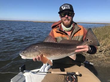 Angler proudly displaying a large Redfish while fishing in a scenic marsh environment.