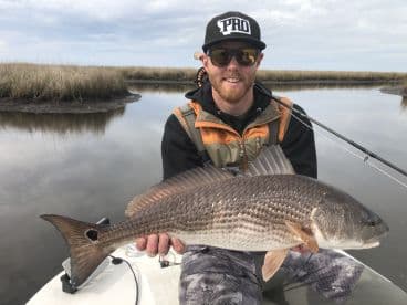 Angler proudly displaying a large Redfish while fishing in a marsh environment.