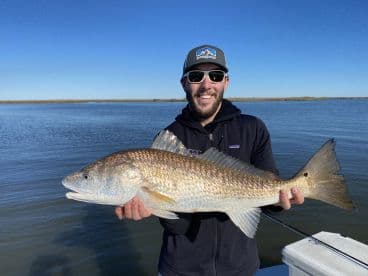 Angler proudly displaying a large Redfish while fishing in a serene coastal environment.