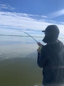 Angler casting a line while fishing in calm waters under a clear blue sky, showcasing a serene fishing environment.