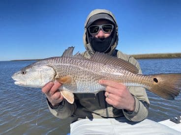 Angler proudly displaying a large Redfish while fishing in a scenic coastal environment.