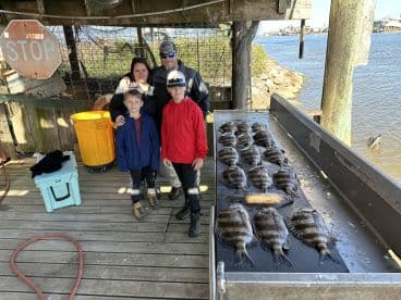 A family poses together at a dock with a display of freshly caught flounder arranged on a cleaning table after a successful fishing trip.