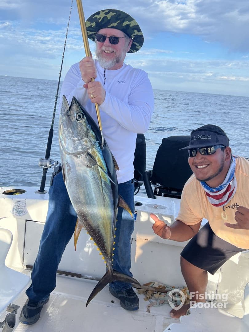 An angler proudly displaying a large Yellowfin Tuna while fishing on a charter boat, with a scenic ocean backdrop.