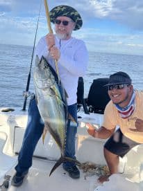 An angler proudly displaying a large Yellowfin Tuna while fishing on a charter boat, with a scenic ocean backdrop.