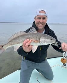 Angler proudly displaying a Redfish while fishing on a calm day, showcasing the thrill of inshore fishing.