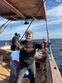A young angler proudly displaying a small fish while fishing on a boat, showcasing a fun day on the water.