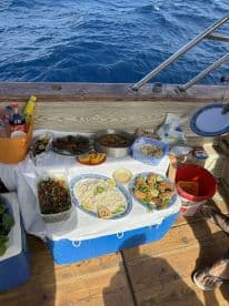A beautifully arranged meal on a fishing boat, featuring fresh seafood, rice, and salads, set against the backdrop of deep blue ocean waters.