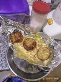 A dish of fish wrapped in foil with grilled lemon slices, likely prepared for a meal.