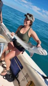 An angler proudly displaying a large shark while fishing on a sunny day in clear blue waters.