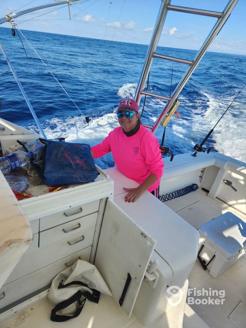 A smiling crew member in a bright pink shirt is seen inside the boat's console area, ready for a fishing adventure on the open sea.