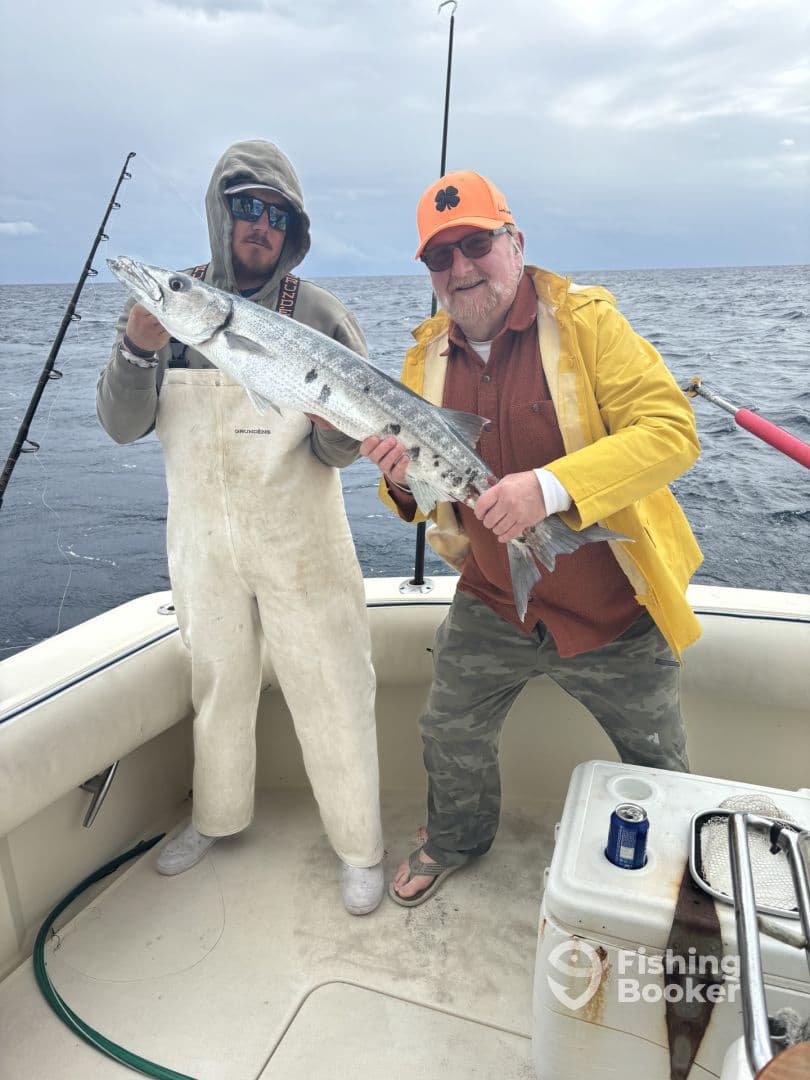 Two anglers proudly displaying a large Barracuda on a fishing charter in open waters.