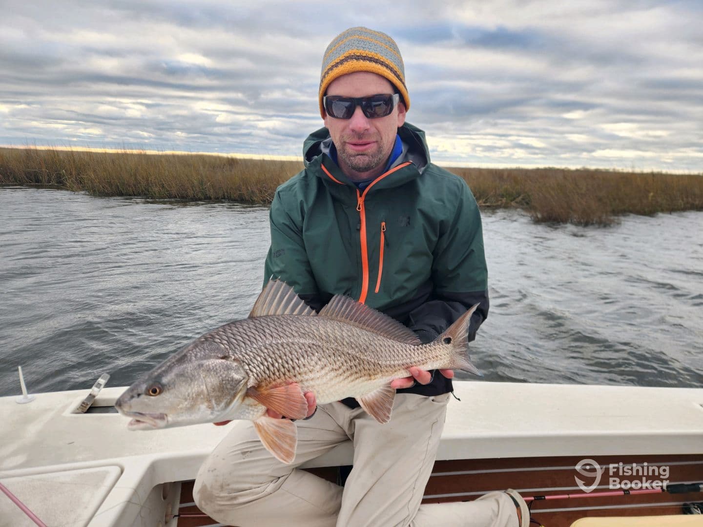An angler proudly displaying a large Redfish while on a boat in a marshy fishing environment.