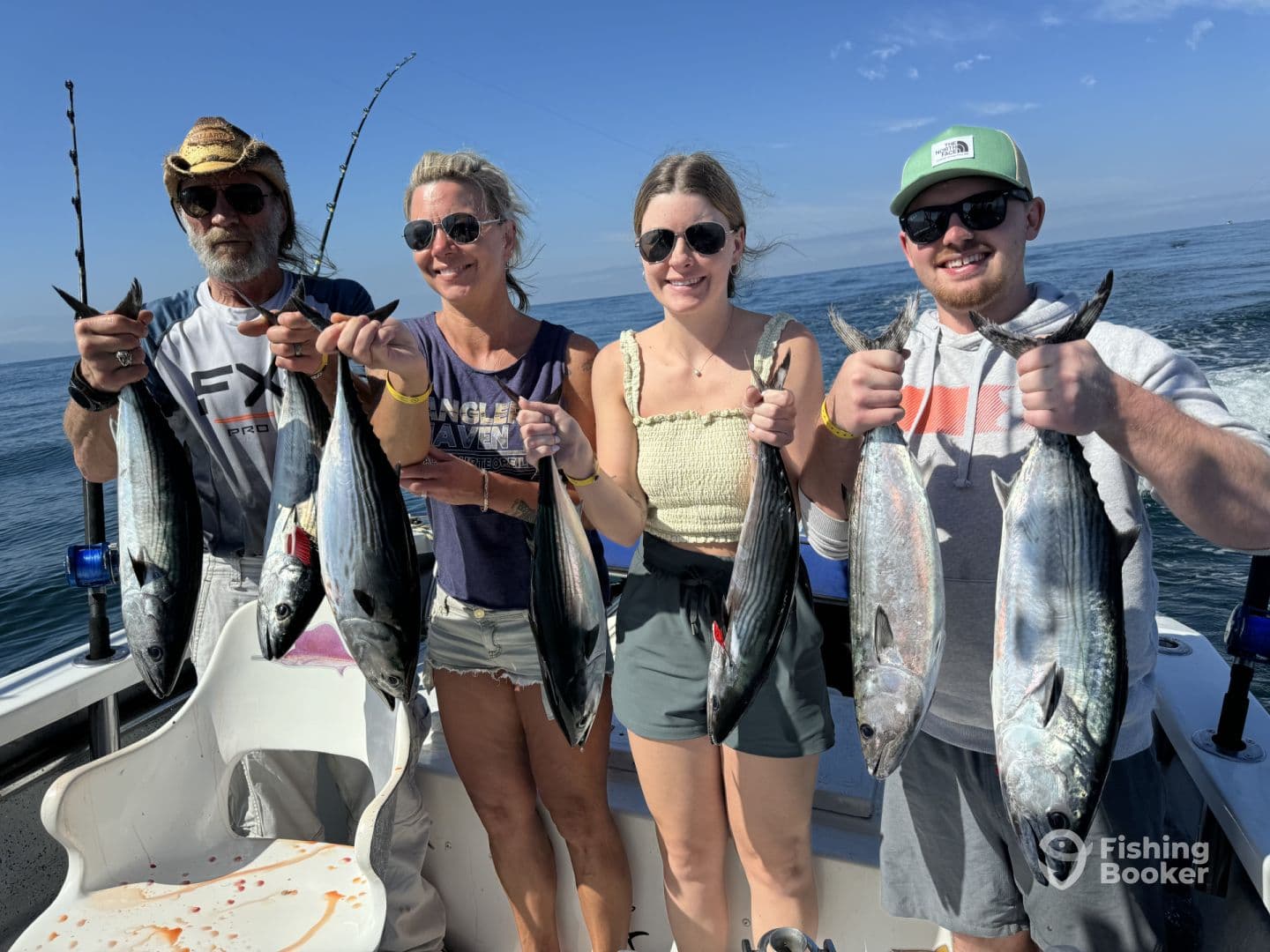 A group of four anglers proudly displaying their catch of several Bonito while out on a fishing trip.