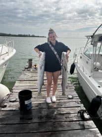 A young woman proudly displaying two large Barracuda on a dock after a successful fishing trip.