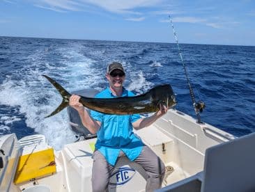 Angler proudly displaying a large Mahi Mahi while aboard a fishing boat in open waters.