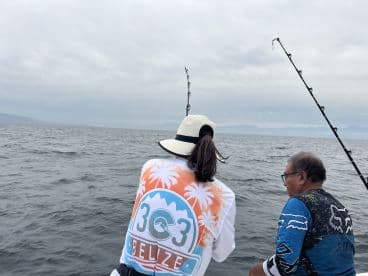 Two anglers engaged in fishing on a boat in Belize, with rods in hand and a cloudy sky overhead.