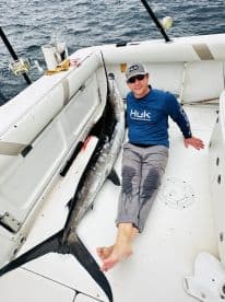 Angler sitting on the boat next to a large Mako Shark, showcasing a successful deep-sea fishing trip.