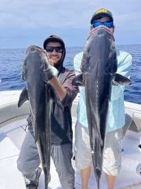 Two anglers proudly displaying their large Cobia catches while out on the open water.