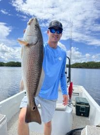 Angler proudly displaying a Redfish while fishing from a boat in a scenic coastal environment.