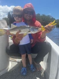A young boy and an adult proudly display a Snook caught while fishing on a sunny day, showcasing a family-friendly fishing experience.