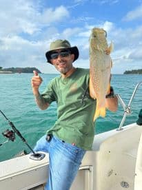 Angler displaying a vibrant Spotted Grouper while fishing from a boat in clear waters, showcasing a successful catch.