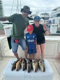 A family proudly displaying their catch of several Grouper species on a cooler after a successful fishing trip.