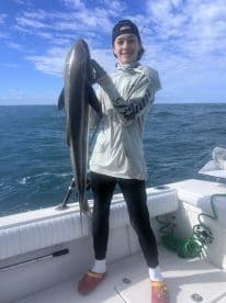 A young angler proudly displaying a large Cobia while fishing on a boat in open waters.