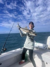 Young angler proudly holding a large fish while fishing on a boat in open waters, showcasing a beautiful day at sea.