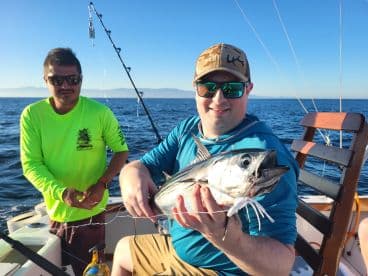 Angler proudly displaying a freshly caught Tuna while fishing on a sunny day at sea.