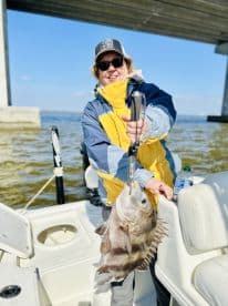 An angler proudly displaying a large Black Drum caught while fishing under a bridge, showcasing a vibrant fishing environment.