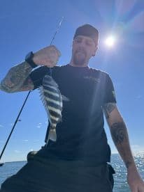 Angler displaying a freshly caught striped fish while fishing on a sunny day, showcasing the excitement of the catch.