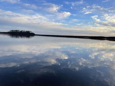 A serene view of a calm water body reflecting the sky, with an island in the distance, ideal for fishing trips.