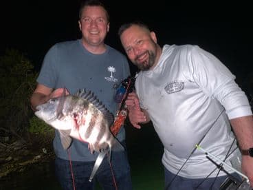 Two anglers proudly displaying a large Sheepshead caught during a night fishing trip.