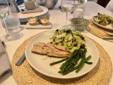 A beautifully arranged plate featuring grilled fish, asparagus, and a fresh salad, set on a dining table with elegant glassware.